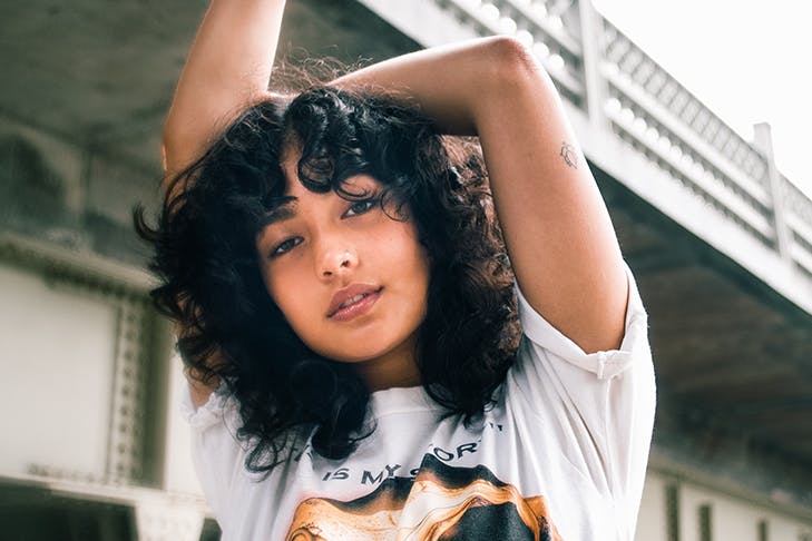 Woman with curly hair standing with her hands in the air.